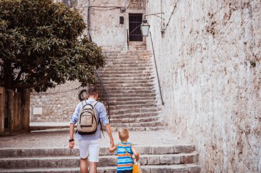 Back view of father and son walking through old town and holding hands. Small boy in the city taking a walk with his father.