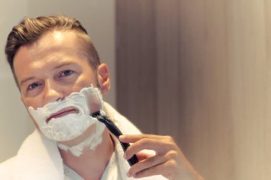 Mid adult man using razor and shaving in the bathroom. Copy space. 