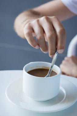 Man enjoying in cup of morning coffee. Hand of a person mixing coffee with a spoon. 