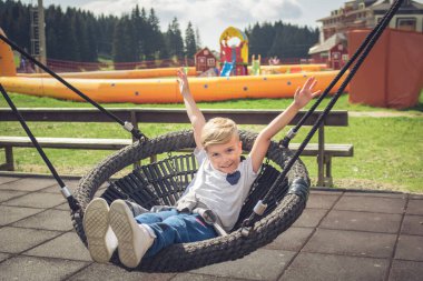 Happy kid having fun while swinging on the playground. 