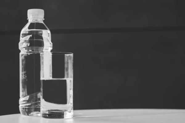 Bottle of pure water and half-full glass on the table. Copy space.