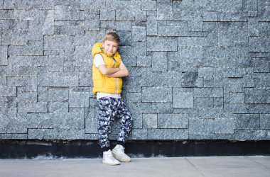 Smiling boy with arms crossed feeling self-confident while leaning on a wall and looking at camera. 