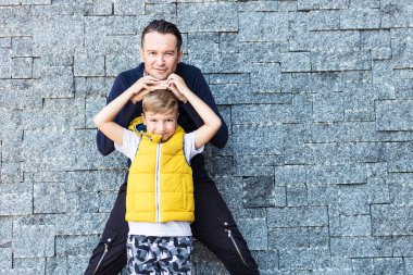 Portrait of happy father and soon standing together against the wall and looking at camera. 