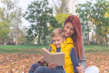 Happy mother and son reading a book while spending a day together in the park. 