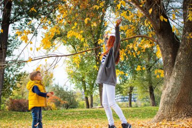 Playful mother and son throwing autumn leaves in the air and having fun together. 