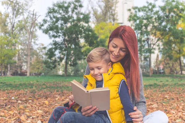 Happy mother and son reading a book while spending a day together in the park. 