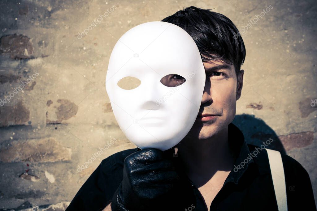 Man holding white mask over half of his face and looking at camera. 