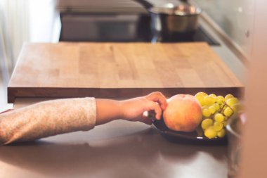 Unrecognizable kid reaching for a fruit in the kitchen.