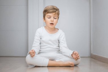 Little boy practicing Yoga in lotus position. Zen-like kid meditating with eyes closed. 