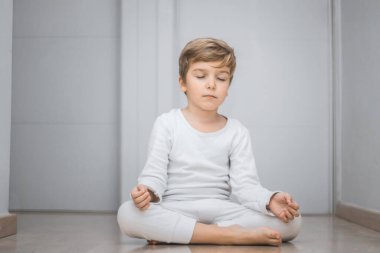 Calm boy meditating in lotus position. Child practicing Yoga with eyes closed. 