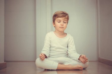 Little boy meditating in lotus position. Child practicing Yoga with eyes closed.