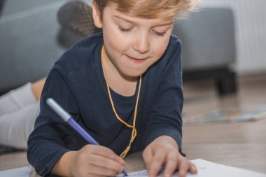 Little boy drawing while lying on the floor at home.