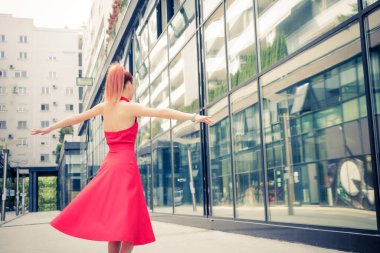 Happy woman in a dress turning around with arms outstretched and having fun in the city.
