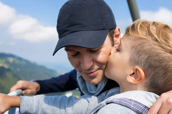 Loving son kissing his father while riding with him on chairlift during vacation.