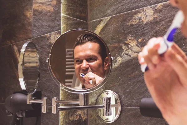 Reflection in a mirror of a man brushing teeth in the bathroom.