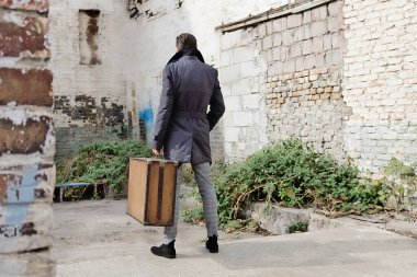 Arka tarafta bavullu bir adam yıkılmış binaların arasında duruyor ve bilinmeyene bakıyor.. 