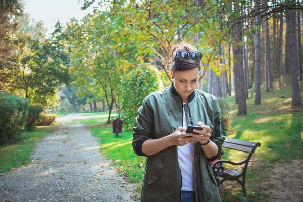 Parkta yürürken cep telefonu ve kısa mesaj kullanan bir kadın. 