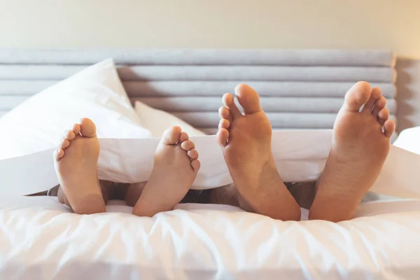 Feet of father and kid lying down on the covered with bed sheet.