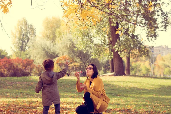 Tasasız anne, baloncuklu değnekle baloncukları üflerken küçük kızı onları yakalamaya çalışıyor.. 
