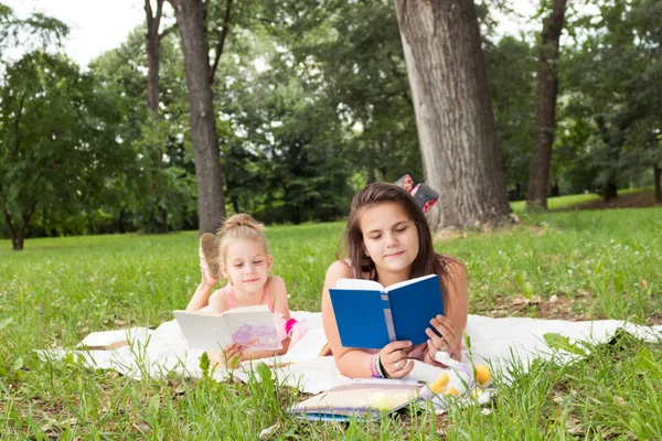 Dwie Małe Dziewczynki Leżące Kocu Czytające Książki Parku — Zdjęcie stockowe