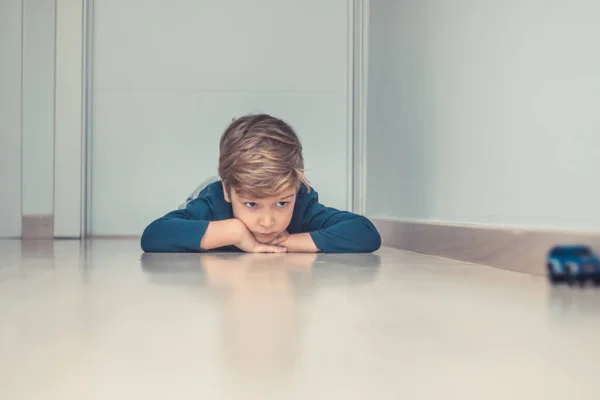 Küçük çocuk koridorda oyuncak arabasıyla oynarken parke zemininde dinleniyor..