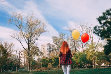 Parkta yürüyen ve renkli balonlar taşıyan bir kadın..