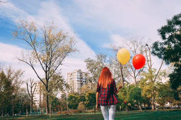 公園を歩いてカラフルな風船を運ぶ女性の背面図 — ストック写真