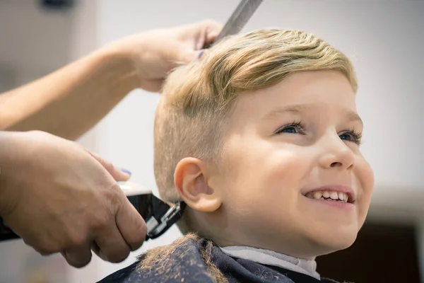 Blond little boy having a haircut at hair salon. 