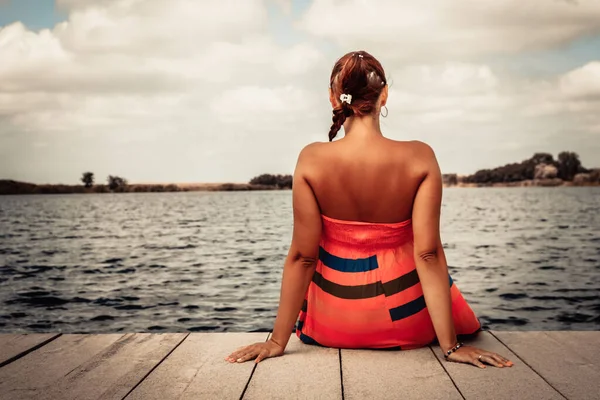 Rear view of woman relaxing on a pier while spending summer day at the beach.