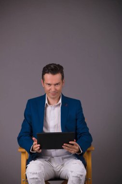 Gri arka plana karşı dijital tablet üzerinde çalışan gülümseyen girişimci kameraya bakıyor. Boşluğu kopyala. 