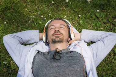 Rahatlamış bir adam izin gününün tadını çıkarıyor ve çimde yatarken kulaklıkla müzik dinliyor.. 