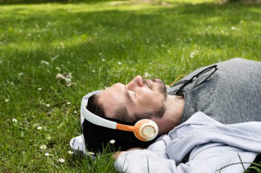 Rahat bir adam çimlere uzanıp gözleri kapalı müzik dinliyor.. 