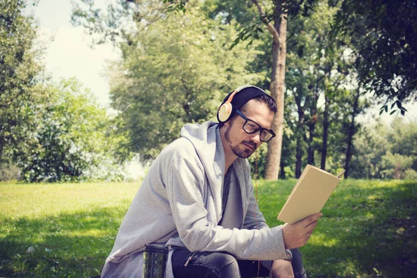 Модний Чоловік Читає Книгу Розслабляється Парку Музикою Над Навушниками — стокове фото