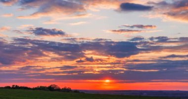  huge bright sun in a red glow sets through the clouds on the horizon at sunset time lapse