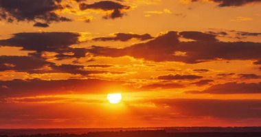  huge bright sun in a red glow sets through the clouds on the horizon at sunset time lapse