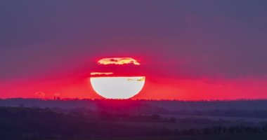  Büyük parlak güneş kırmızı bir parıltıyla ufuk üzerindeki bulutların arasından batıyor gün batımında zaman akıp gidiyor.