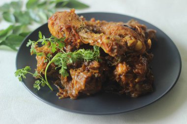 Kerala style dry chicken roast. Chicken cooked in a spicy gravy of onion tomatoes and spices served with chicken leg pieces on top. Shot on white background.
