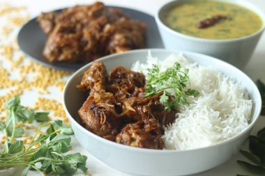 Kerala style dry chicken roast and lentil curry prepared with fenugreek leaves served with basmati rice. A healthy combination meal called rice with chicken and methi dal. Shot on white background