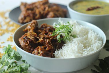 Kerala style dry chicken roast and lentil curry prepared with fenugreek leaves served with basmati rice. A healthy combination meal called rice with chicken and methi dal. Shot on white background