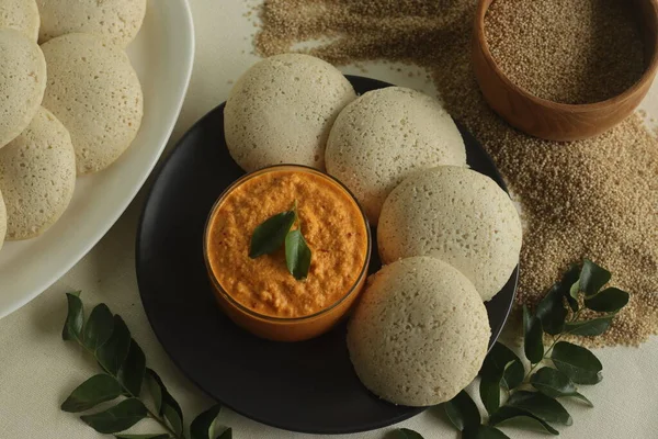 Steamed Little millet cakes or little millet idli. Made with fermented batter of little millet, lentils. Served with coconut chutney. Shot on white background along with little millet in wooden bowl