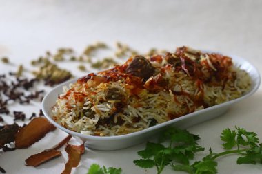 Koyun Biryani. Baharatlarla pişirilmiş hafif baharatlı ghee pilavı ile bol karamelli soğan ve yoğurt içinde marine edilmiş koyun eti karışımı bir yemek. Etrafta bir sürü baharat var.