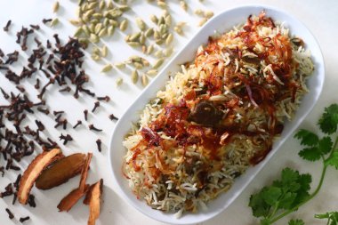 Koyun Biryani. Baharatlarla pişirilmiş hafif baharatlı ghee pilavı ile bol karamelli soğan ve yoğurt içinde marine edilmiş koyun eti karışımı bir yemek. Etrafta bir sürü baharat var.