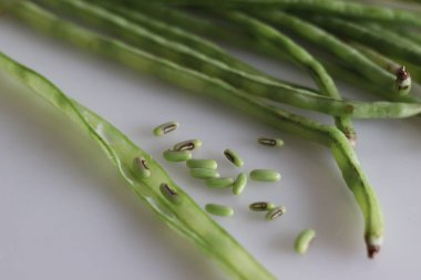 Bir sürü uzun fasulye kabuğundan çıkmış, masaya yayılmış. Ayrıca uzun ömürlü inek bezelyesi, kuşkonmaz fasulyesi, yılan fasulyesi ya da Çin uzun fasulyesi olarak da bilinir. Beyaz arkaplanda çekilen