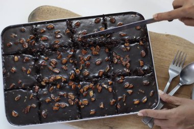 Teksas pastasını dilimliyorum. Tereyağlı ve çikolatalı pasta fırın kutusunun içindeki dikdörtgen parçalara bölünmüş. Fırından yeni çıktı. Beyaz arkaplanda çekilen