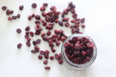 Cam bir şişede kurumuş yaban mersini. Beyaz arka planda çekilmiş. Kurumuş yaban mersinleri etrafa saçılmış.