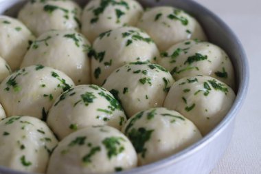 Akşam yemeği hamuru yuvarlak bir teneke içinde fırına gitmeye hazır hale getirir. Tereyağı, doğranmış kişniş ve otlarla kaplı. Beyaz arkaplanda çekilen.