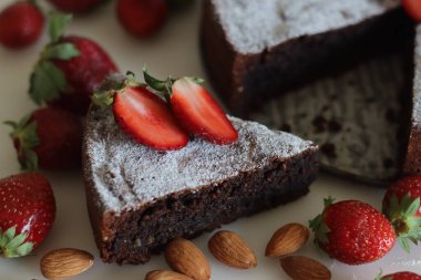 Slices of Torta caprese. Chocolate and almond cake. A yummy chocolaty flourless cake from the Capri island, Italy. Sprinkled with sugar powder. Shot along with fresh strawberries on white background.