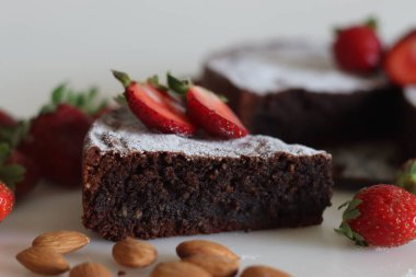 Slices of Torta caprese. Chocolate and almond cake. A yummy chocolaty flourless cake from the Capri island, Italy. Sprinkled with sugar powder. Shot along with fresh strawberries on white background.