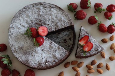Sliced Torta caprese. Chocolate and almond cake. A yummy chocolaty flourless cake from the Capri island, Italy. Sprinkled with sugar powder. Shot along with fresh strawberries on white background.