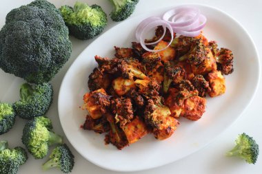 Tandır paneer brokoli. Süzme peynir küpleri ve yoğurt, baharat ve havada kızartılmış brokoli çiçekleri. Sağlıklı bir başlangıç mı yoksa akşam yemeği mi? Beyaz arkaplanda çekilen.